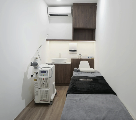 A well-lit treatment room featuring a medical device, a washbasin, and a consultation bed.
