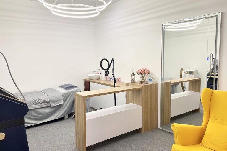 A well-lit beauty treatment room featuring a massage table, a mirror, and aesthetic equipment.