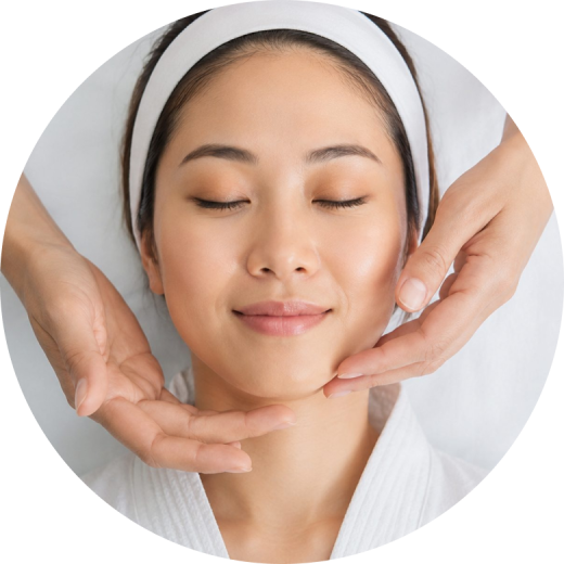 A woman receiving a facial treatment with a professional's hands gently massaging her jawline.