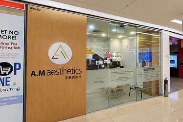 The exterior view of an aesthetics clinic with a glass entrance and a wooden sign displaying the clinic's logo.