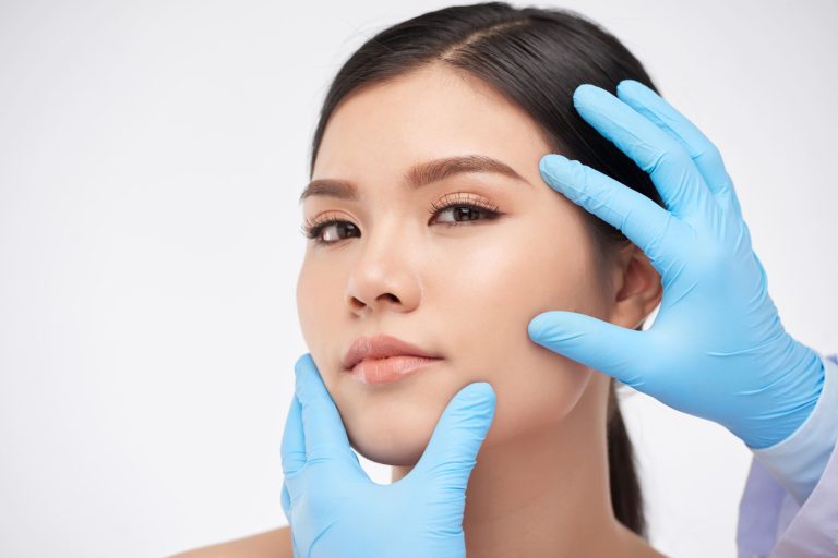 A young woman receiving a facial examination with gloved hands in a clinical setting.