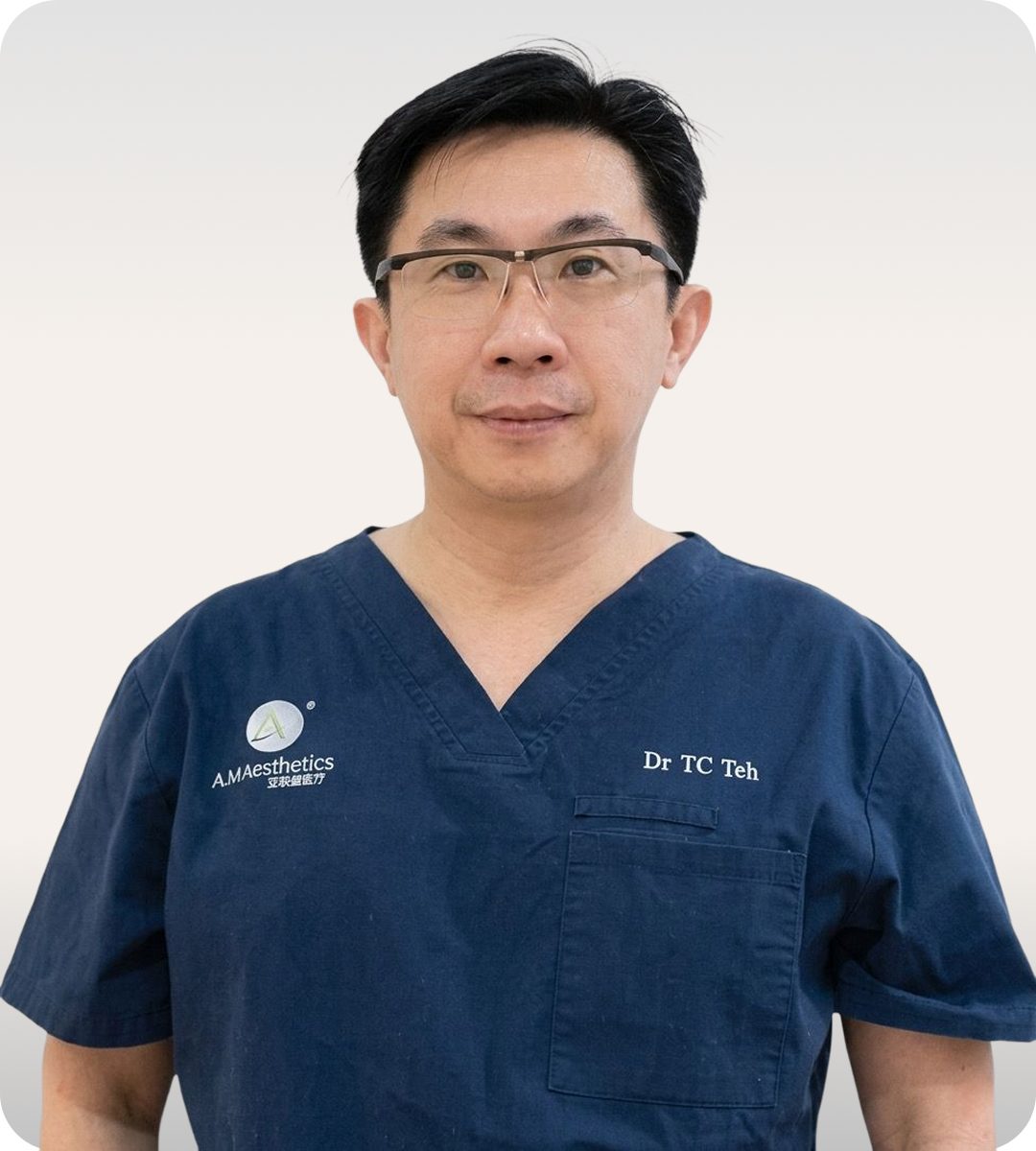 A doctor in dark blue scrubs with glasses, looking directly at the camera.
