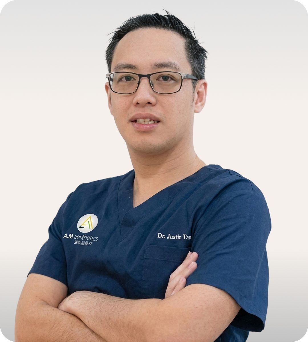A medical professional in dark scrubs with arms crossed, standing confidently against a neutral background.