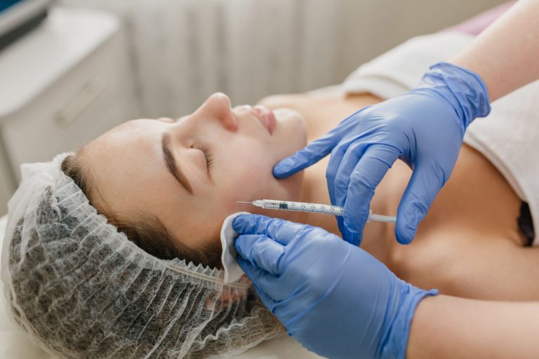 A professional aesthetician performing a cosmetic injection procedure on a woman's cheek in a clinic.