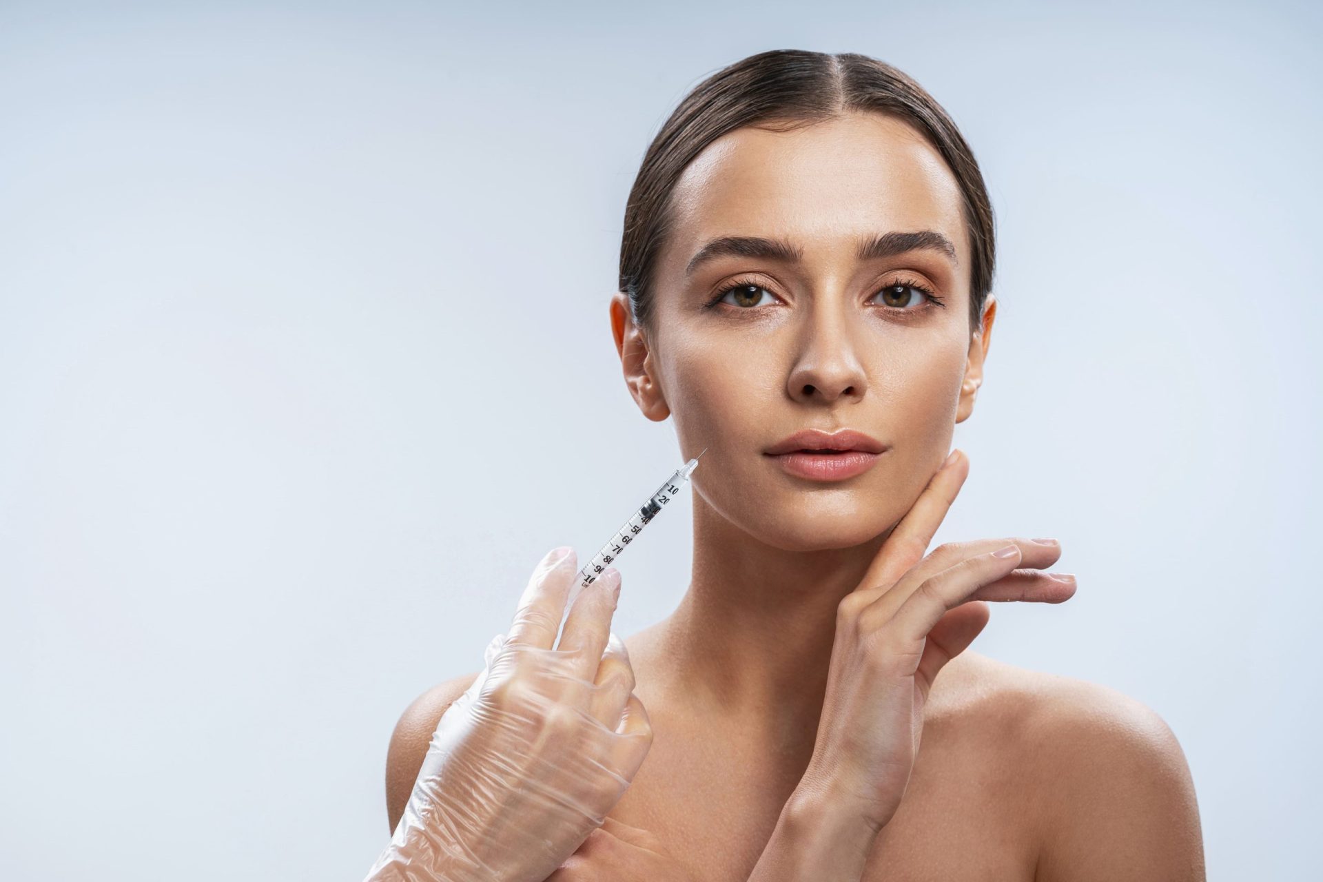 A woman receiving a facial injection with a syringe in a clinical setting, highlighting a procedure for aesthetic enhancement.