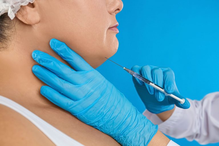 A close-up of a cosmetic procedure being performed on a woman's chin using a syringe by a professional wearing blue gloves.