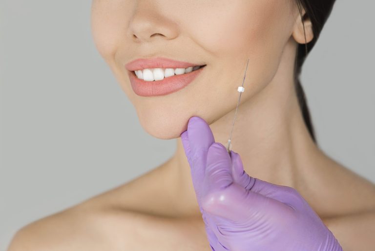 A close-up of a woman's face during a facelift procedure, with a syringe being held near her chin.