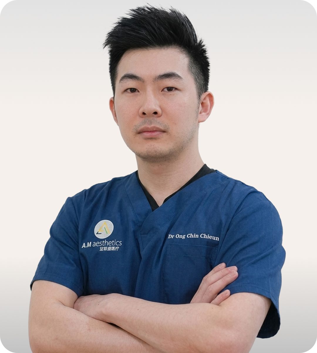 A doctor in blue scrubs with crossed arms, posing against a white background.