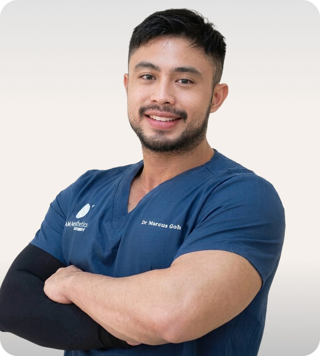 A smiling healthcare professional in blue scrubs with arms crossed, representing a confident and approachable demeanor in a clinical setting.