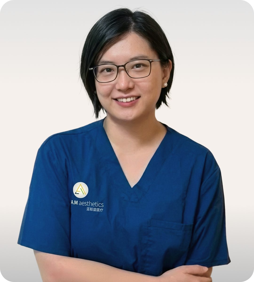 A professional doctor in blue scrubs smiling for the camera in a clinical setting.