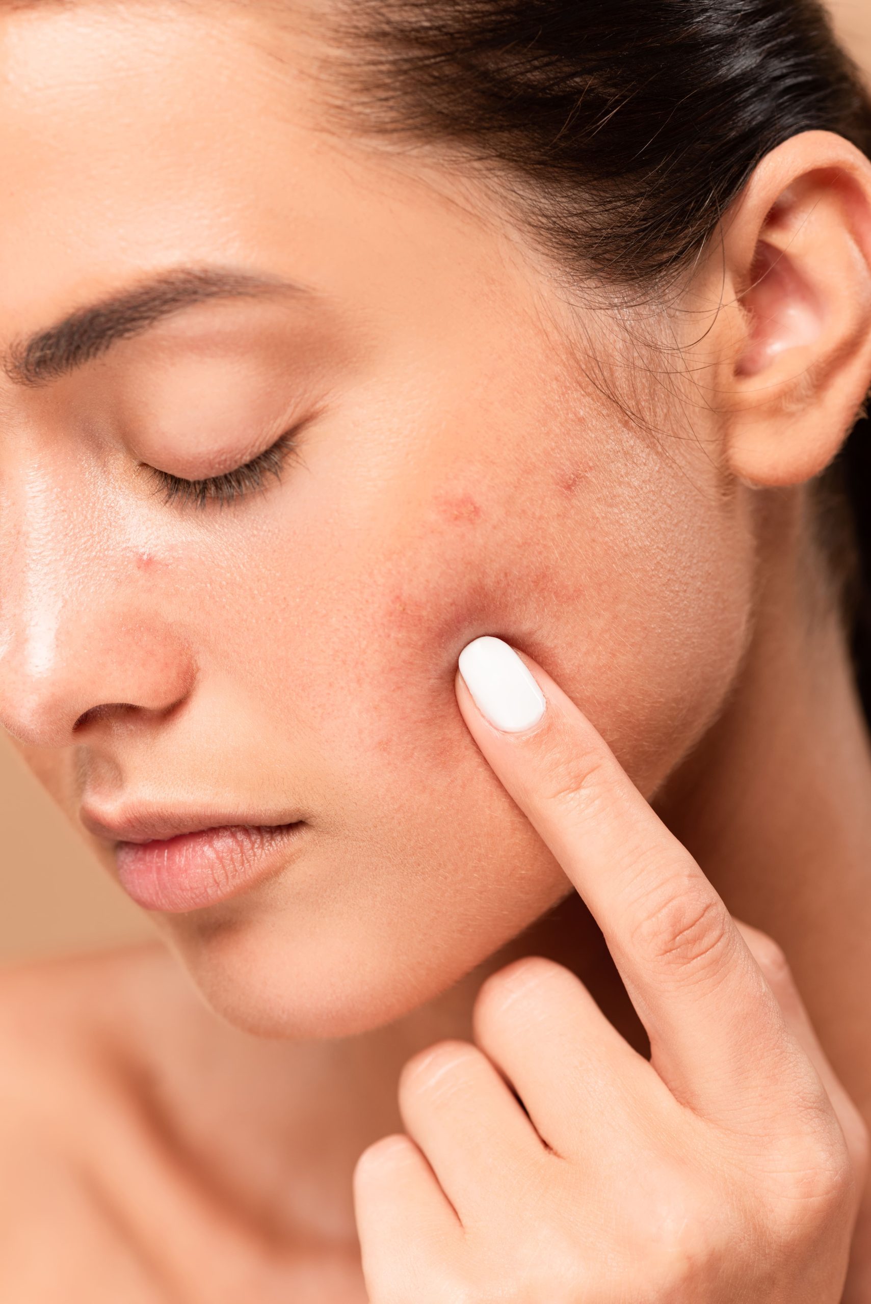 A young woman examining her skin and pointing at blemishes during a skincare routine.