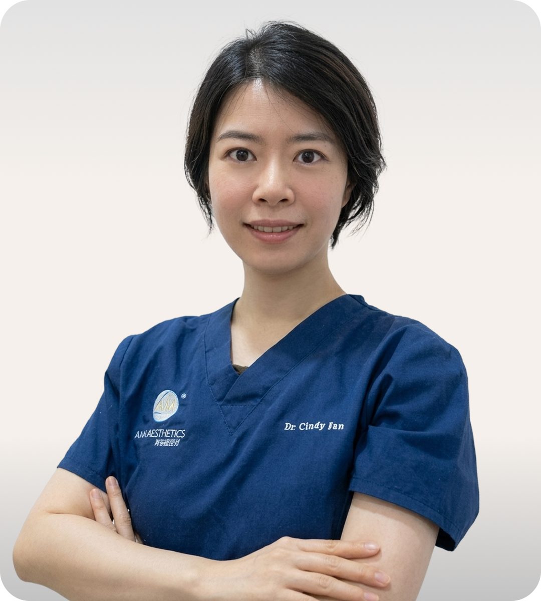 A medical professional wearing a navy blue uniform, smiling and posing with arms crossed in a clinic setting.