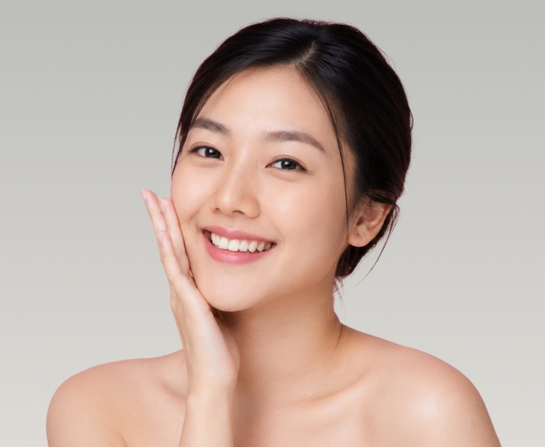 A happy woman showing her clear skin while touching her face, representing the benefits of medical facial treatments.