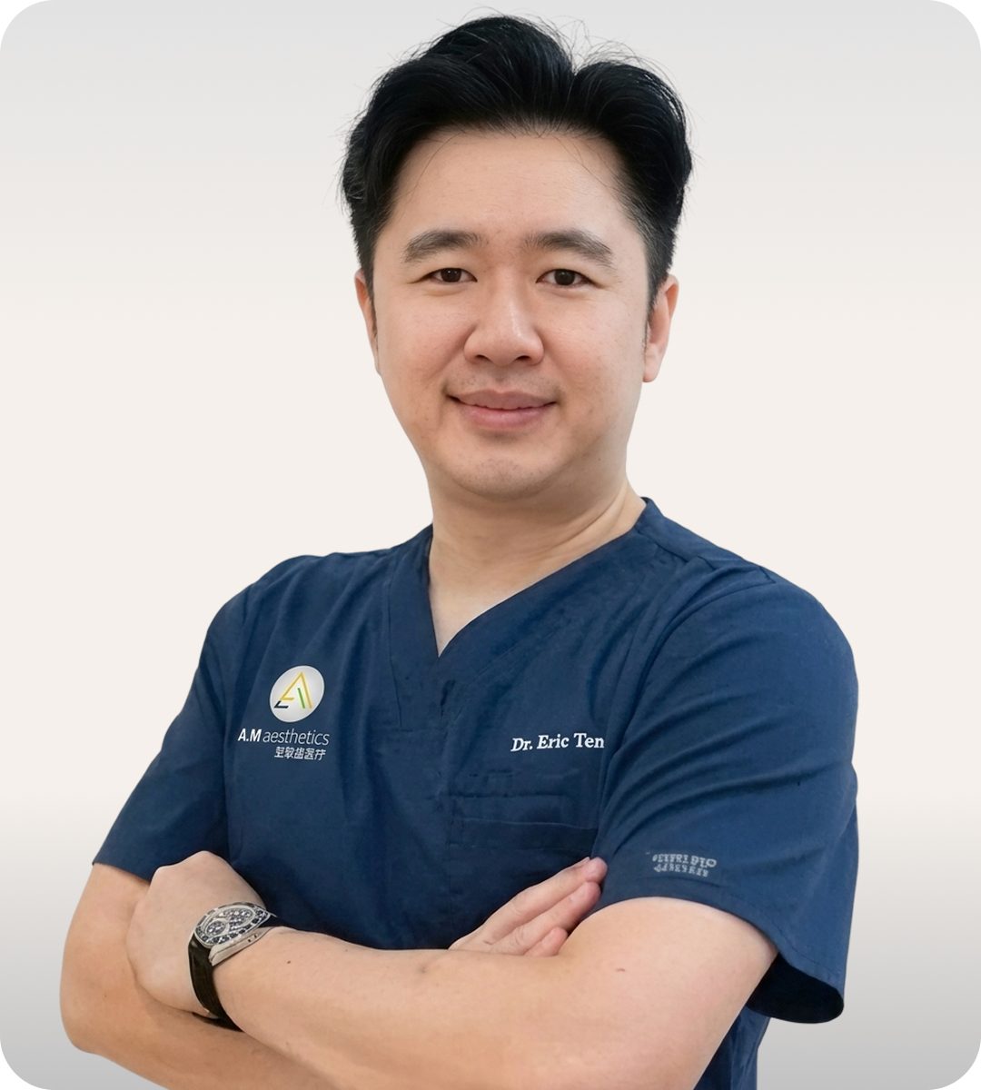 A healthcare professional wearing a navy blue medical scrubs with arms crossed, standing against a light background.
