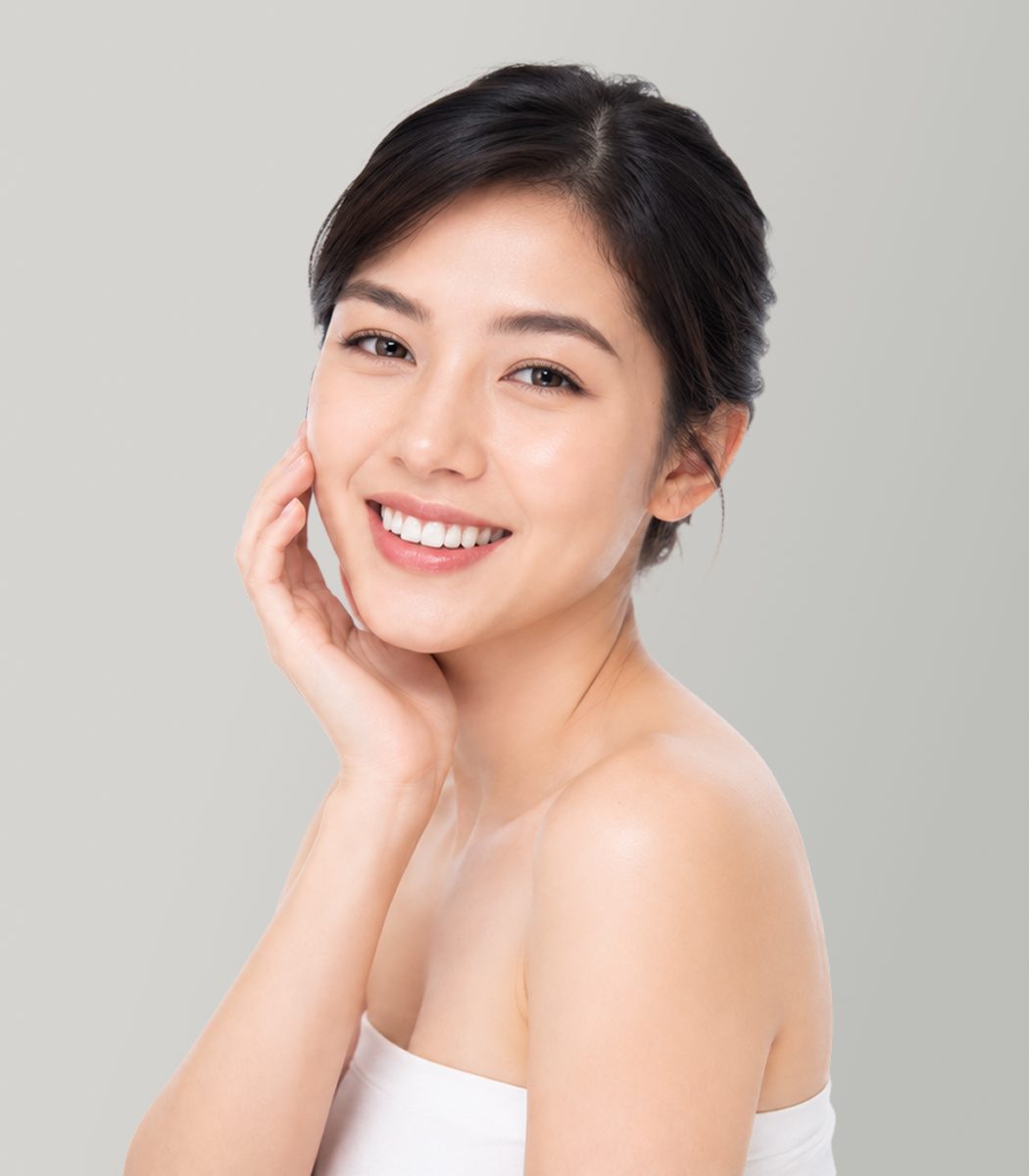 A smiling woman gently touching her face with one hand, showcasing a radiant smile and clear skin.