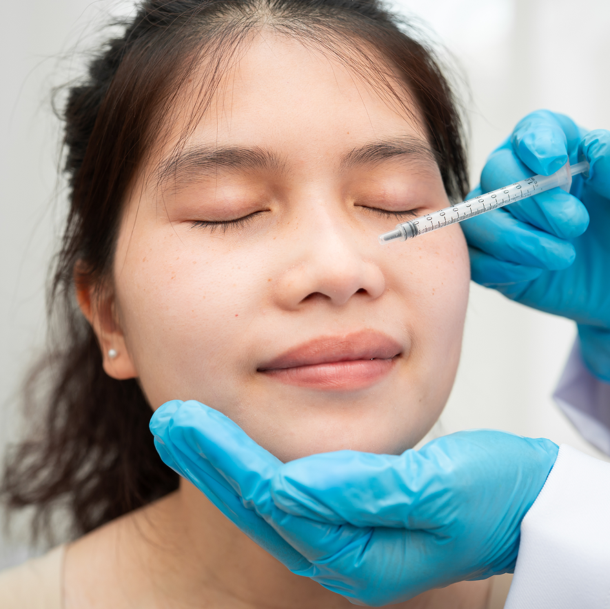 A young woman receiving a beauty treatment involving a needle, administered by a professional wearing blue gloves.