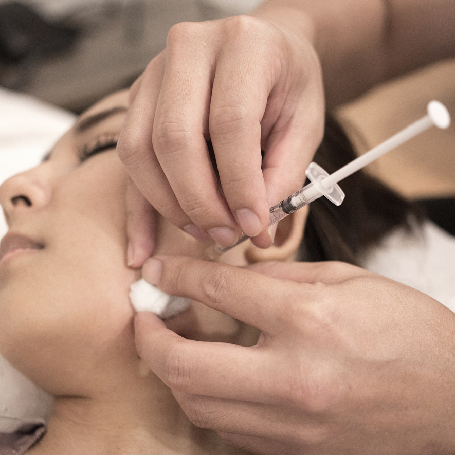 A close-up view of a cosmetic injection being administered to a patient's cheek in a clinical setting.