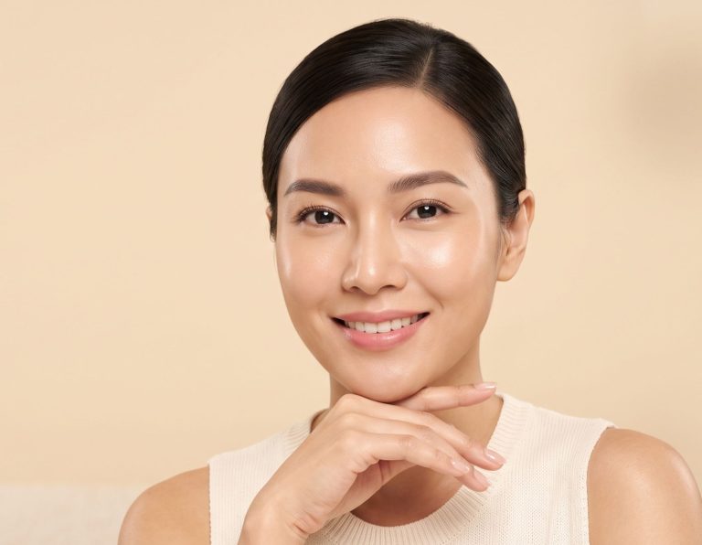A smiling woman with smooth skin posed gently resting her chin on her hand.